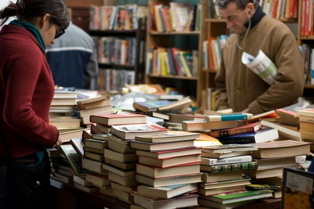 "Woman and Man Standing Beside Piles of Books"