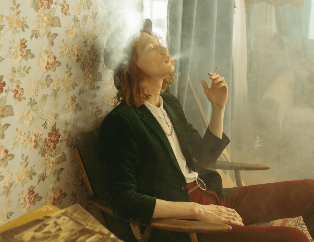 Man in Green Blazer Sitting on Brown Wooden Chair while Smoking